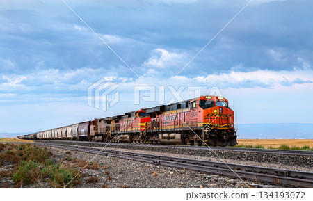 Moccasin, Montana - August 20, 2025: A BNSF freight train, locomotive ET44AC 6424, travels through the rural plains of central Montana under a dramatic cloudy sky Moccasin, Montana - August 20, 2025: A BNSF freight train, locomotive ET44AC 6424, travels through the rural plains of central Montana under a dramatic cloudy sky 134193072