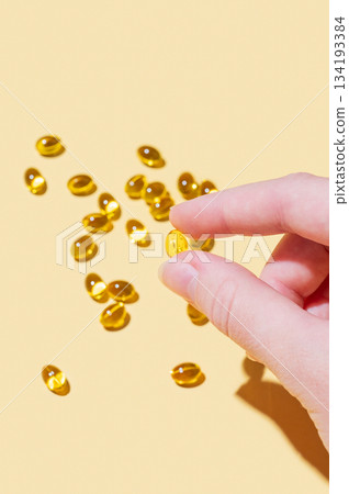 A hand holding a soft capsule containing D3 on a yellow background with shadow. A hand holding a soft capsule containing D3 on a yellow background with shadow. 134193384