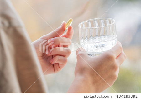 A close-up of a person's hands holding yellow softgel in one palm and a glass of water in the other. 134193392