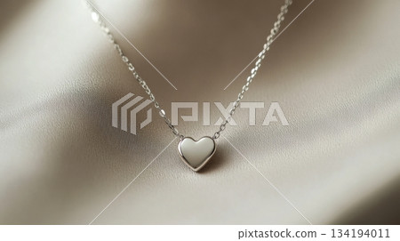 Elegant silver necklace with heart pendant displayed on soft fabric background 134194011