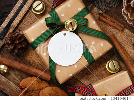 Blank paper gift tag on wrapped Christmas present near rustic wooden decor, holiday mockup Blank paper gift tag on wrapped Christmas present near rustic wooden decor, holiday mockup 134194614