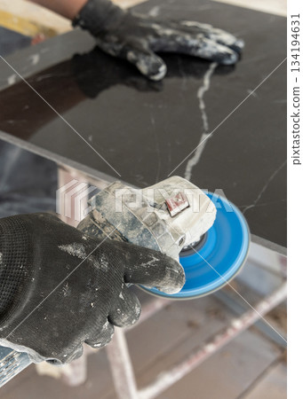 Craftman in grey shirt grinds black ceramic tile using an sand grinder. Handy men at work, hands closeup Craftman in grey shirt grinds black ceramic tile using an sand grinder. Handy men at work, hands closeup 134194631