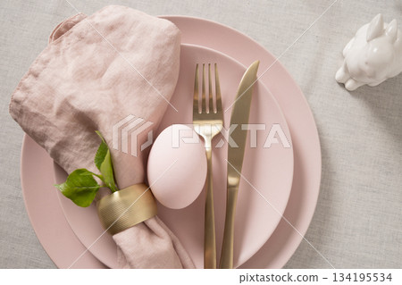 Easter table setting with pastel pink egg, gold cutlery and linen napkin on soft pink plate. Elegant spring decor. Easter table setting with pastel pink egg, gold cutlery and linen napkin on soft pink plate. Elegant spring decor. 134195534