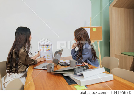 Busy office women meet for work, analyzing market data, collaborating as a focused team, planning strategy with financial charts, documents, and laptop on conference table. Busy office women meet for work, analyzing market data, collaborating as a focused team, planning strategy with financial charts, documents, and laptop on conference table. 134195658