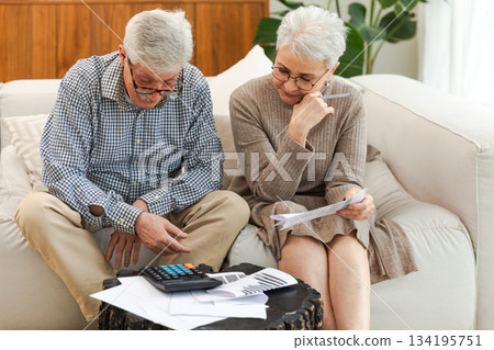 Middle aged senior couple sit with laptop and paper document. Older mature man woman reading paper bill pay online at home managing bank finances calculating taxes planning loan debt pension payment 134195751