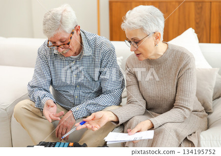 Middle aged senior couple sit with laptop and paper document. Older mature man woman reading paper bill pay online at home managing bank finances calculating taxes planning loan debt pension payment 134195752