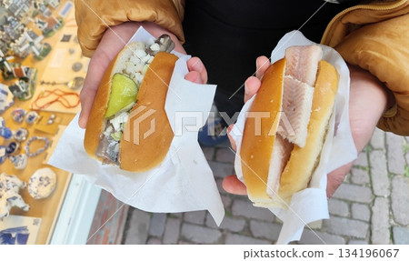 Raw eel and herring in a bun in hands. Dutch herring in Volendam Netherlands fish street food Raw eel and herring in a bun in hands. Dutch herring in Volendam Netherlands fish street food 134196067