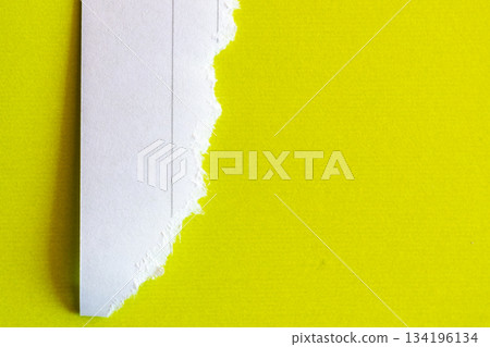 Ripped white paper with lined texture on a bright yellow background. The torn edge creates a contrast between the two colors. 134196134