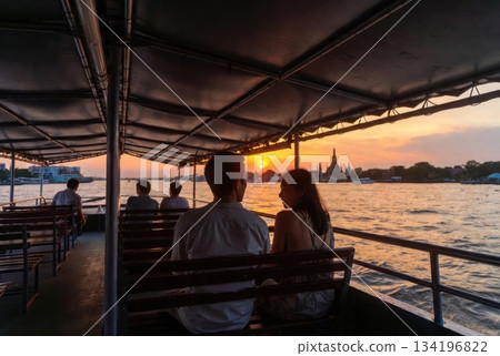 Over-the-shoulder view of foreign travelers on a Thai ferry looking toward Wat Arun at sunset 134196822