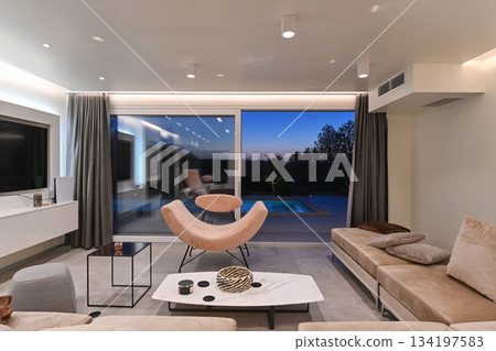 Elegant modern living room with designer lounge chair, panoramic glass doors, sunset view, and poolside terrace in a luxury contemporary home interior Elegant modern living room with designer lounge chair, panoramic glass doors, sunset view, and poolside terrace in a luxury contemporary home interior 134197583