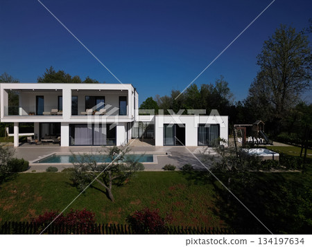 Modern luxury villa with pool, terraces, and clean minimalist architecture captured by drone. Bright sunny day, surrounding greenery, and contemporary outdoor living areas 134197634