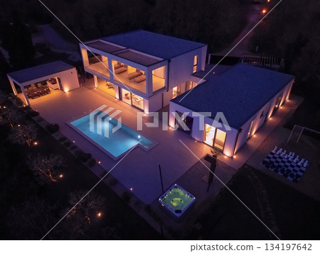Modern luxury villa illuminated at night with pool, terraces, and contemporary architecture. Warm lighting and elegant outdoor living create a stylish and sophisticated atmosphere Modern luxury villa illuminated at night with pool, terraces, and contemporary architecture. Warm lighting and elegant outdoor living create a stylish and sophisticated atmosphere 134197642