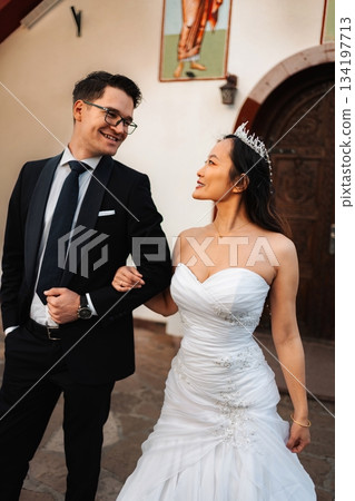Interracial wedding couple smiling while walking arm in arm Interracial wedding couple smiling while walking arm in arm 134197713
