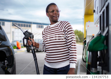 Adult woman refueling car at gas station looking away 134197753