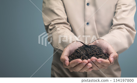 Person's cupped hands holding a mound of rich, dark earth, symbolizing growth, sustainability, environmental care, and the foundations of future development and investment 134197800