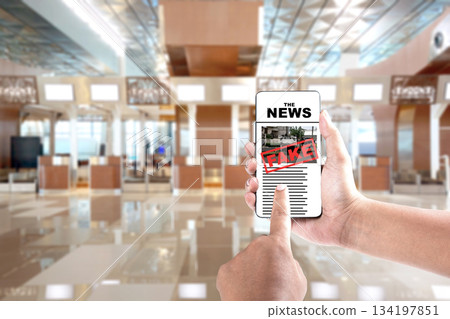 Hand holding a smartphone displaying a news article marked as "FAKE". Represents the spread of misinformation and the importance of verifying news sources. Concept of Hoax news 134197851