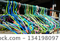 A Colorful Array of Plastic Clothes Hangers Hanging Outdoors on a Metal Rail in Sunlight 134198097