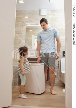 Father and daughter placing dirty clothes into a laundry hamper at home Father and daughter placing dirty clothes into a laundry hamper at home 134199539