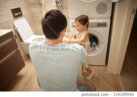 Father and daughter sorting clothes from the laundry basket in bathroom Father and daughter sorting clothes from the laundry basket in bathroom 134199540