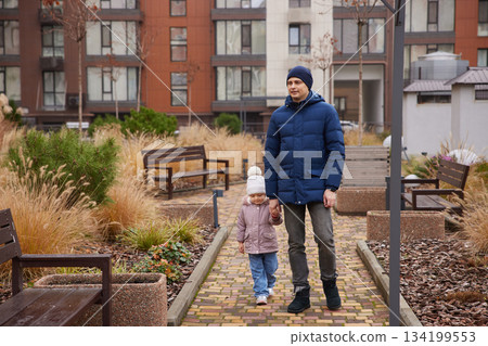 Father and young daughter walking together holding hands in a modern urban park 134199553