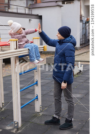 Father and daughter bonding, giving a high five, and playing outdoors during winter Father and daughter bonding, giving a high five, and playing outdoors during winter 134199558