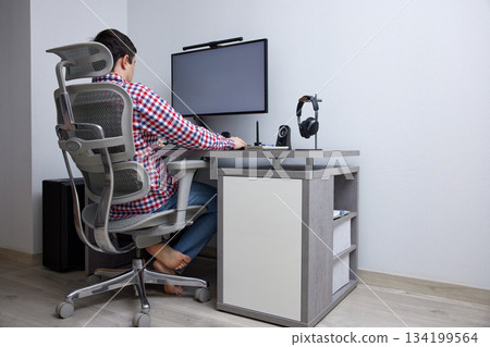 Man focusing on computer screen while sitting in an ergonomic chair at a modern desk 134199564