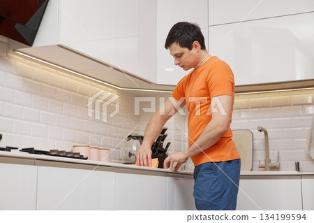 Man cleaning white kitchen countertop with an orange sponge in a modern kitchen Man cleaning white kitchen countertop with an orange sponge in a modern kitchen 134199594