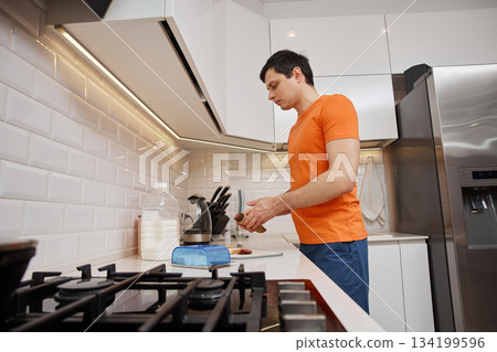 Man slicing sausage for breakfast toast in bright domestic kitchen 134199596