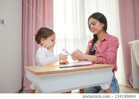 Mother and daughter cutting designs from paper with scissors for an art project Mother and daughter cutting designs from paper with scissors for an art project 134199604