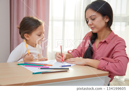 Mother and cute little daughter drawing with colored pencils, engaging in creative home learning 134199605