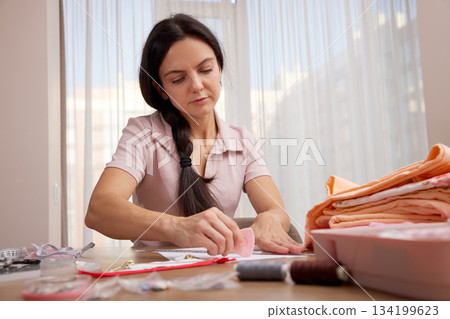 Woman focusing on drawing a fashion sketch at a table with sewing supplies 134199623