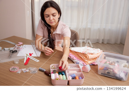 Woman carefully hand sewing fabric with a needle on a wooden table Woman carefully hand sewing fabric with a needle on a wooden table 134199624