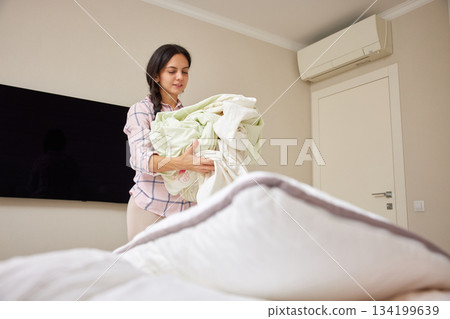 Woman standing in bedroom carrying fresh clean bedding linen Woman standing in bedroom carrying fresh clean bedding linen 134199639