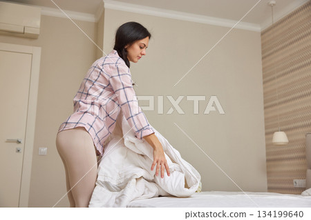 Woman making her bed, tidying up bedroom for a fresh start to the day 134199640