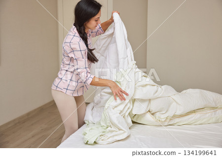 Woman making her bed, tidying up bedroom for a fresh start to the day Woman making her bed, tidying up bedroom for a fresh start to the day 134199641