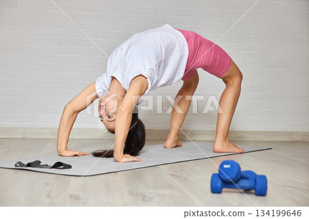 Woman performing a yoga bridge pose on a mat during home fitness routine 134199646