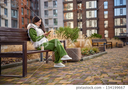Woman sitting on a park bench, texting on her mobile phone 134199667