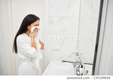 Young woman drying her face with a soft white towel in a clean bathroom Young woman drying her face with a soft white towel in a clean bathroom 134199689