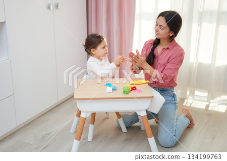 Mother and daughter playing with colorful play-doh modeling clay at a small table 134199763