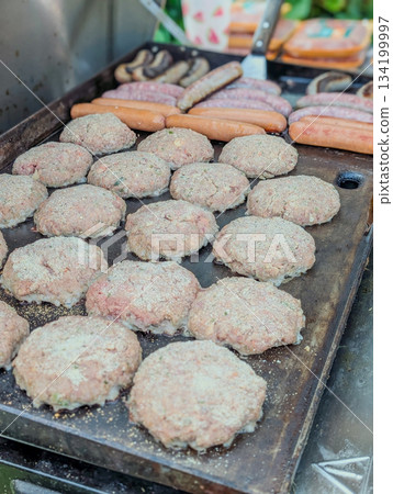 Chef grilling appetising beef burgers  and bratwurst outdoors 134199997