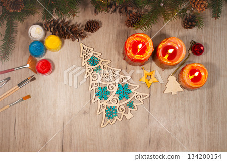 Painted wooden toy Christmas tree with brushes, paints, spruce branches, pinecones and candles on table Painted wooden toy Christmas tree with brushes, paints, spruce branches, pinecones and candles on table 134200154