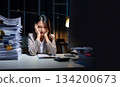 A businesswoman with a sad expression on her face, surrounded by a huge pile of documents, holding her head 134200673