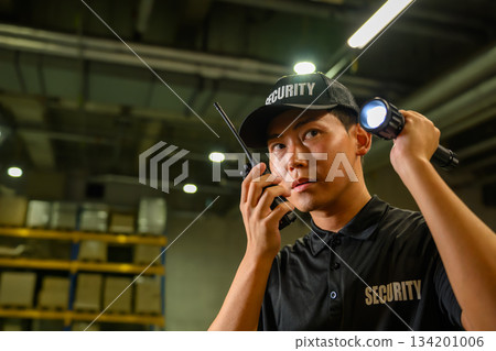 Security guard with walkie-talkie and flashlight in warehouse 134201006
