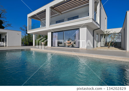 Modern luxury villa with pool, terrace, and minimalist architecture on a sunny day. Clean lines, large windows, and outdoor living spaces create a stylish contemporary home setting Modern luxury villa with pool, terrace, and minimalist architecture on a sunny day. Clean lines, large windows, and outdoor living spaces create a stylish contemporary home setting 134202829