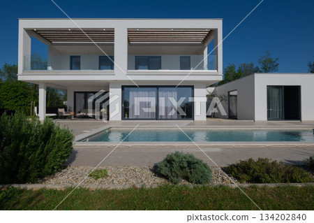 Modern luxury villa with pool, terrace, and minimalist architecture on a sunny day. Clean lines, large windows, and outdoor living spaces create a stylish contemporary home setting Modern luxury villa with pool, terrace, and minimalist architecture on a sunny day. Clean lines, large windows, and outdoor living spaces create a stylish contemporary home setting 134202840