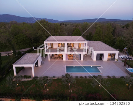 Modern luxury villa illuminated at night with pool, terraces, and contemporary architecture. Warm lighting and elegant outdoor living create a stylish and sophisticated atmosphere 134202850