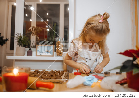 Child makes cookies in a home kitchen during festive season with family around Child makes cookies in a home kitchen during festive season with family around 134203222