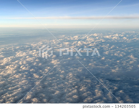Aerial view of fluffy clouds and blue sky from an airplane window Aerial view of fluffy clouds and blue sky from an airplane window 134203505