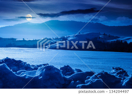 beautiful winter landscape with snow covered rolling hills under dark sky at night. majestic mountains in full moon light. frosty countryside scenery. backdrop for fiction art or mystery concepts 134204497