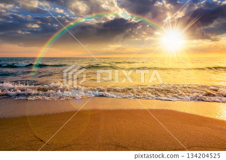 sand beach at the sea for summer vacation concept. beautiful sunset at perfect coast with calm waves and clouds on sky in evening light. scenic landscape for timeless nostalgia book cover with rainbow 134204525